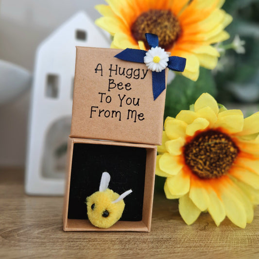 Small plush bee toy in a box with a card and sunflowers in the background